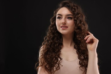 Photo of Beautiful young woman with long curly brown hair on black background, space for text