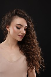 Photo of Beautiful young woman with long curly brown hair on black background