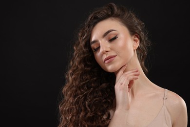 Photo of Beautiful young woman with long curly brown hair on black background, space for text