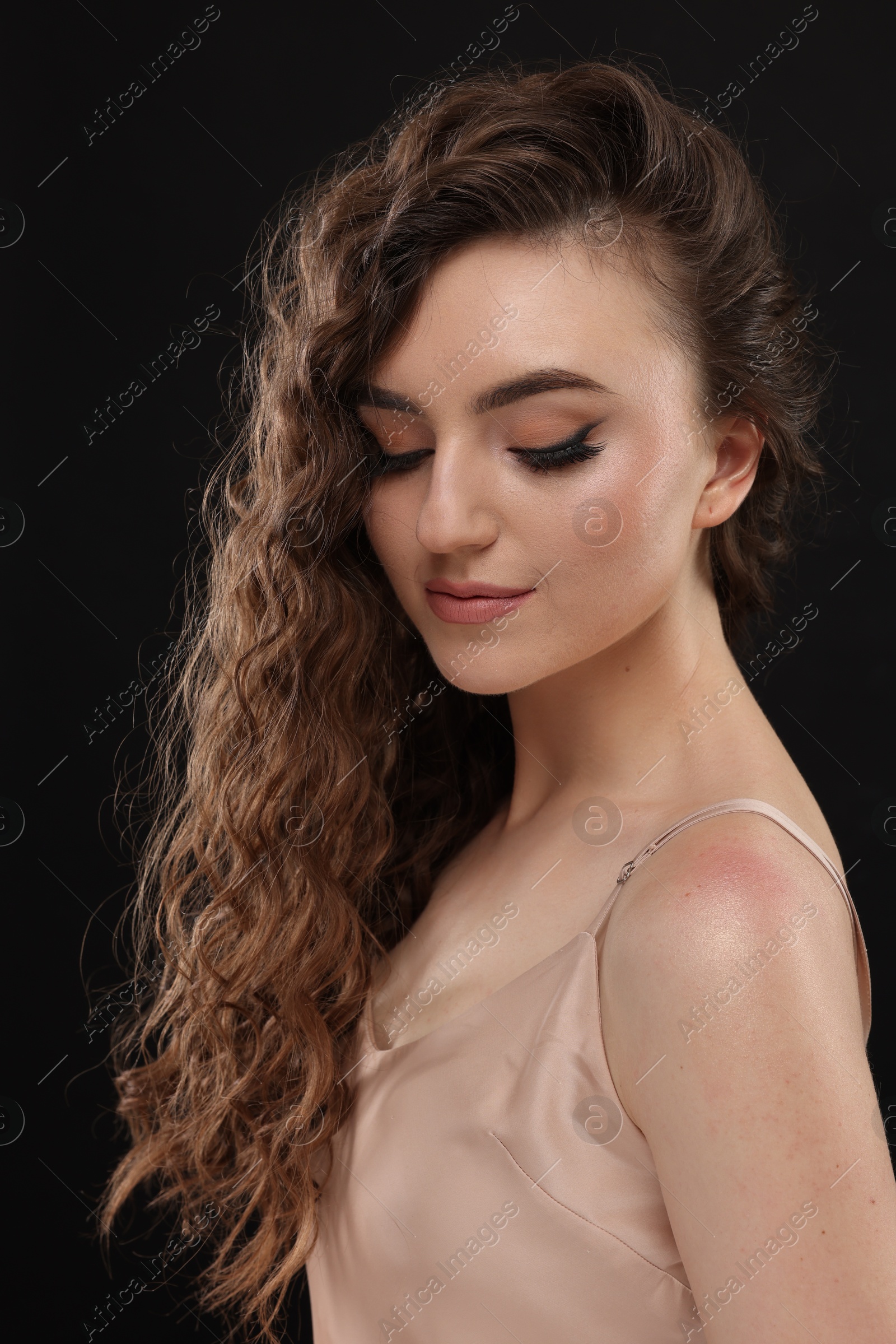 Photo of Beautiful young woman with long curly brown hair on black background