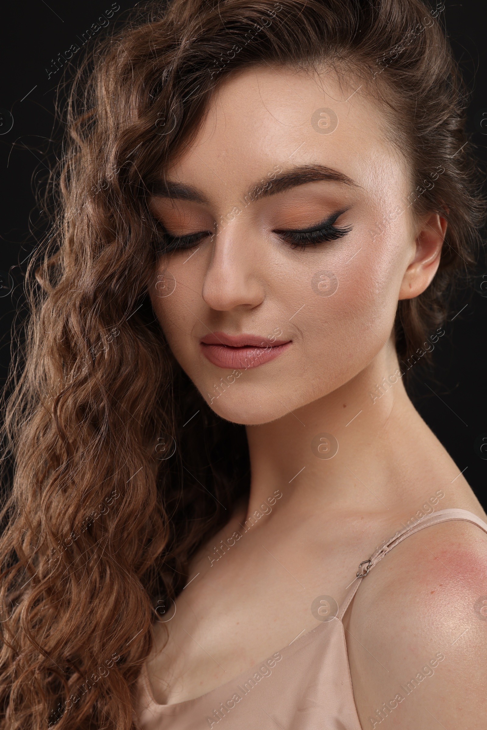 Photo of Beautiful young woman with long curly brown hair on black background, closeup