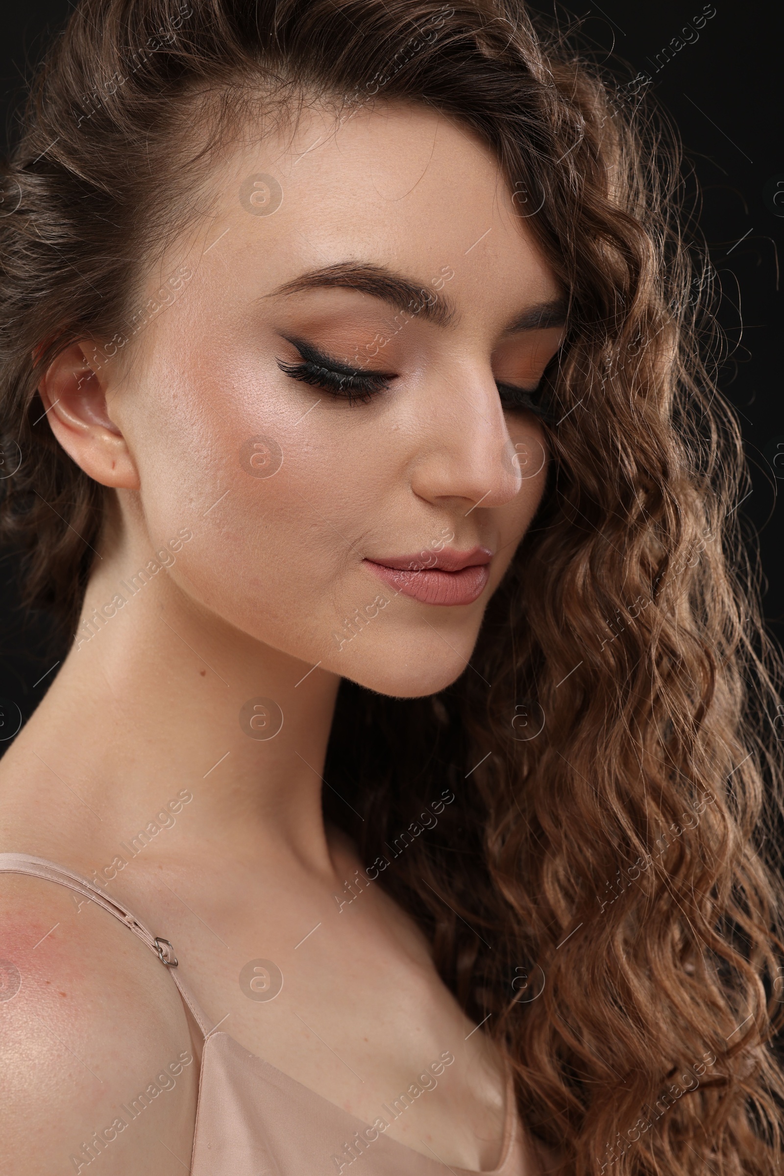 Photo of Beautiful young woman with long curly brown hair on black background, closeup