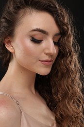 Photo of Beautiful young woman with long curly brown hair on black background, closeup