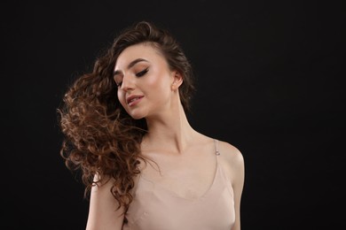 Photo of Beautiful young woman with long curly brown hair on black background, space for text