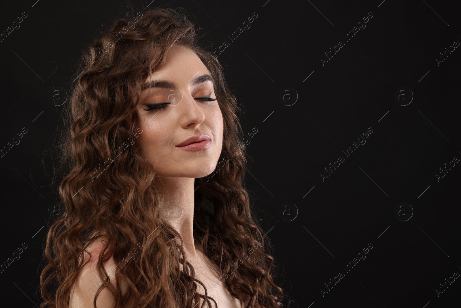 Photo of Beautiful young woman with long curly brown hair on black background. Space for text