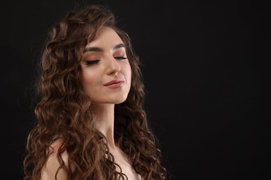 Photo of Beautiful young woman with long curly brown hair on black background. Space for text