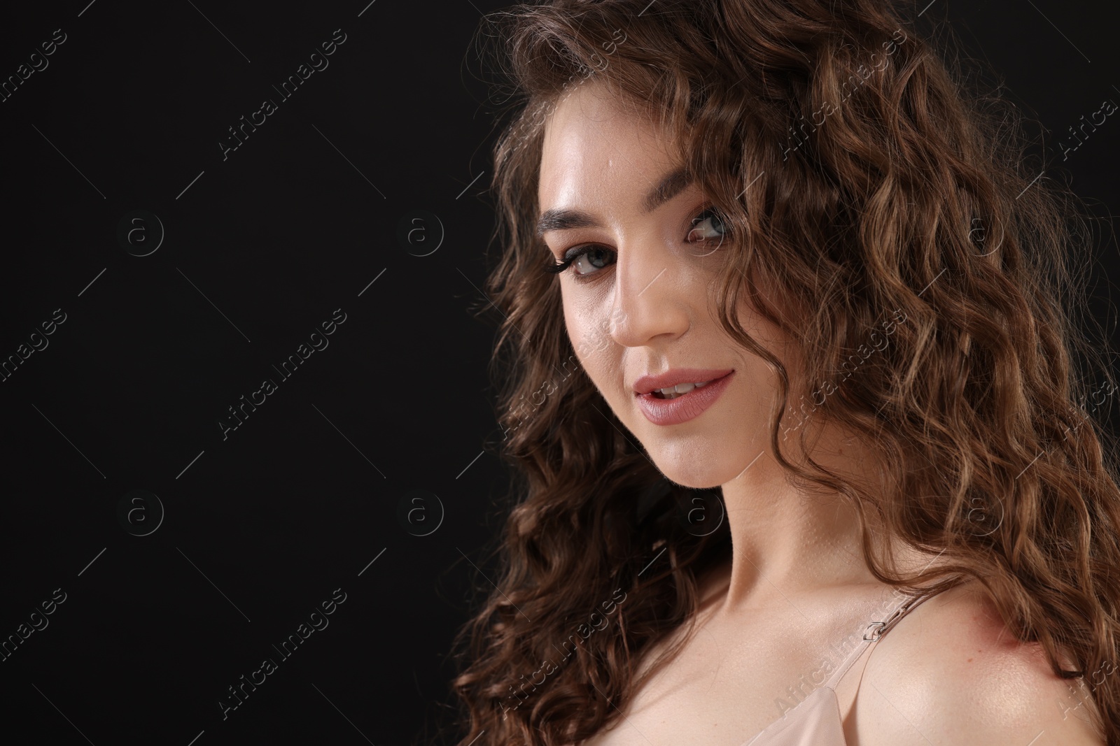 Photo of Beautiful young woman with long curly brown hair on black background, closeup. Space for text