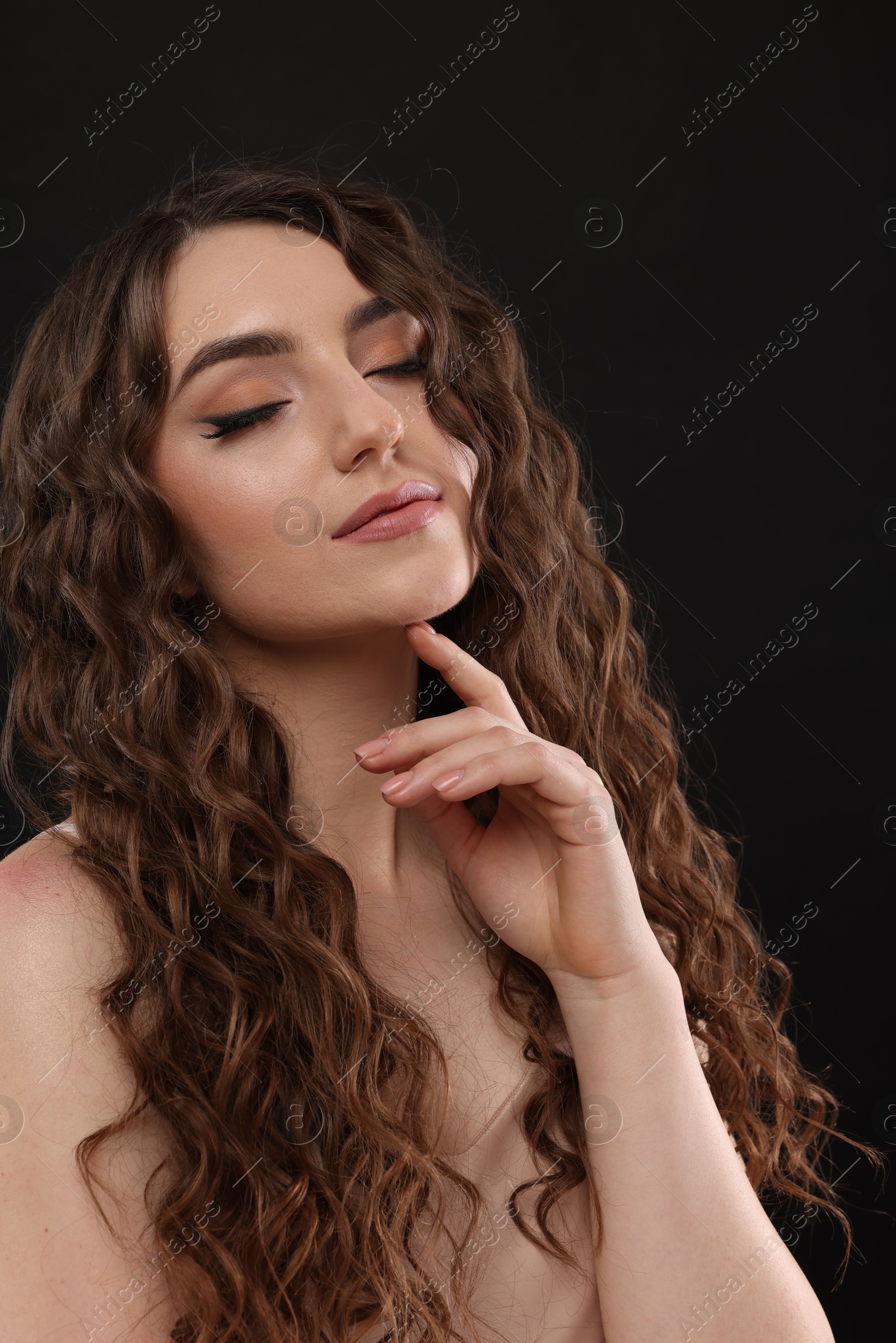 Photo of Beautiful young woman with long curly brown hair on black background