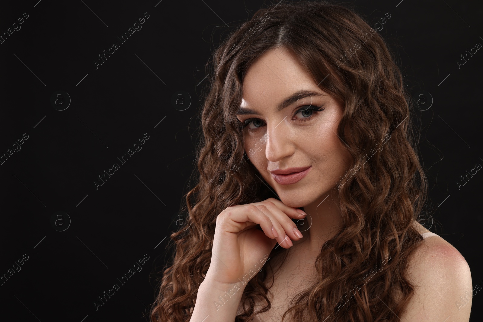 Photo of Beautiful young woman with long curly brown hair on black background, space for text