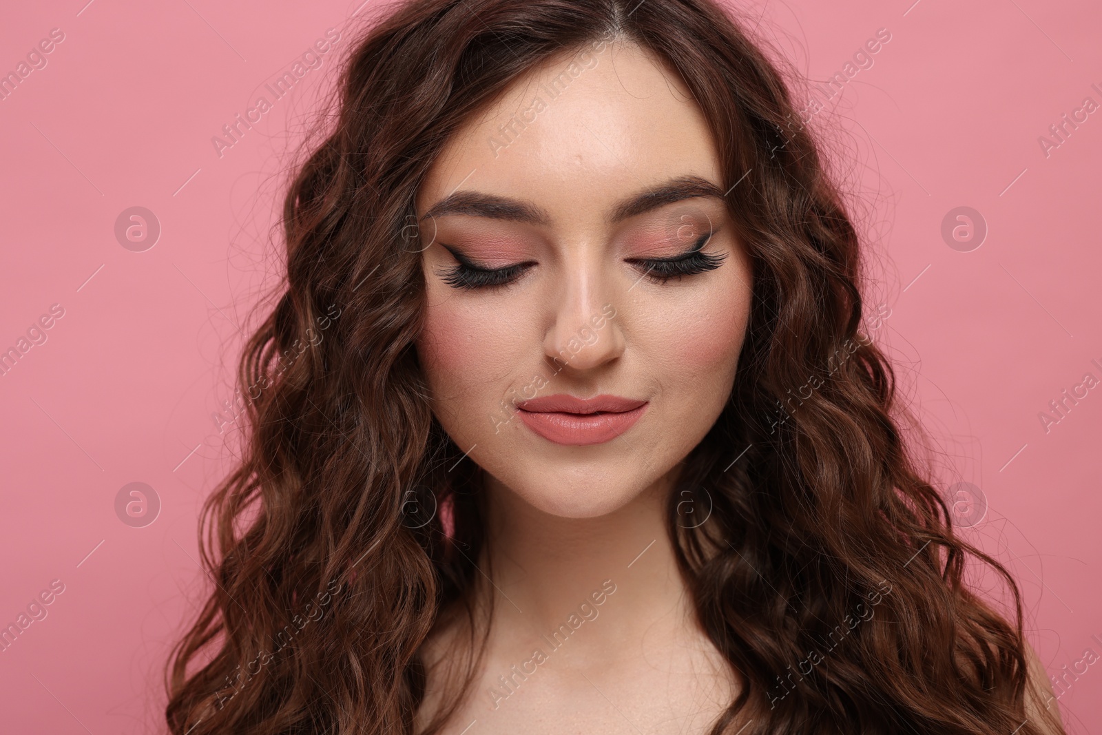 Photo of Beautiful young woman with long curly brown hair on pink background, closeup