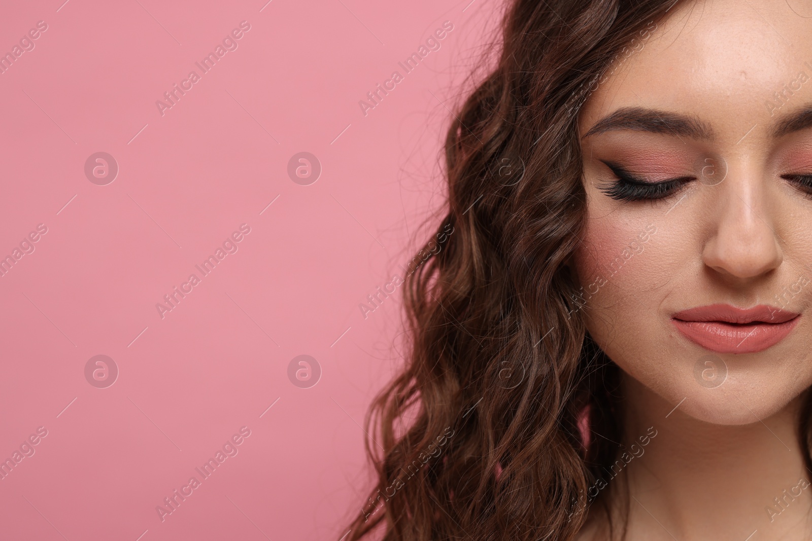 Photo of Beautiful young woman with long curly brown hair on pink background, closeup. Space for text