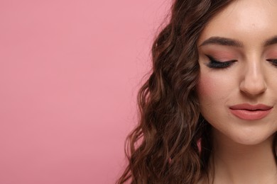 Photo of Beautiful young woman with long curly brown hair on pink background, closeup. Space for text