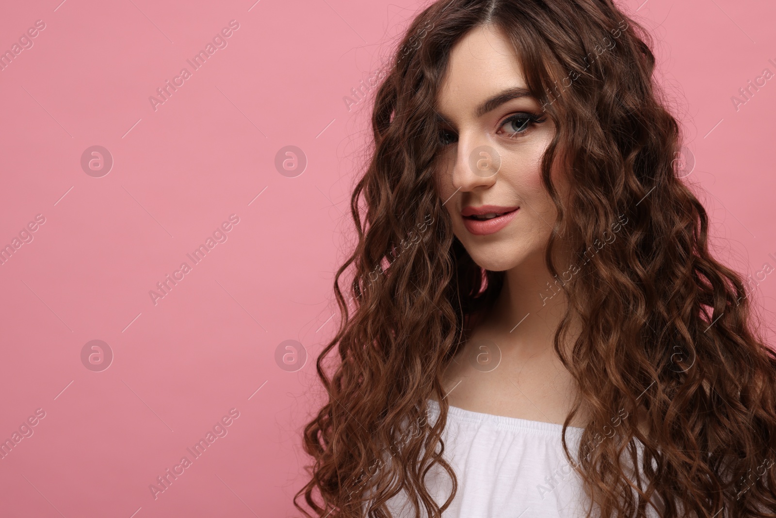 Photo of Beautiful young woman with long curly brown hair on pink background, space for text