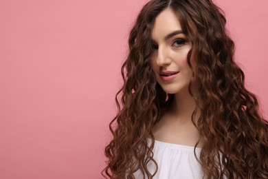 Photo of Beautiful young woman with long curly brown hair on pink background, space for text