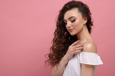 Photo of Beautiful young woman with long curly brown hair on pink background, space for text