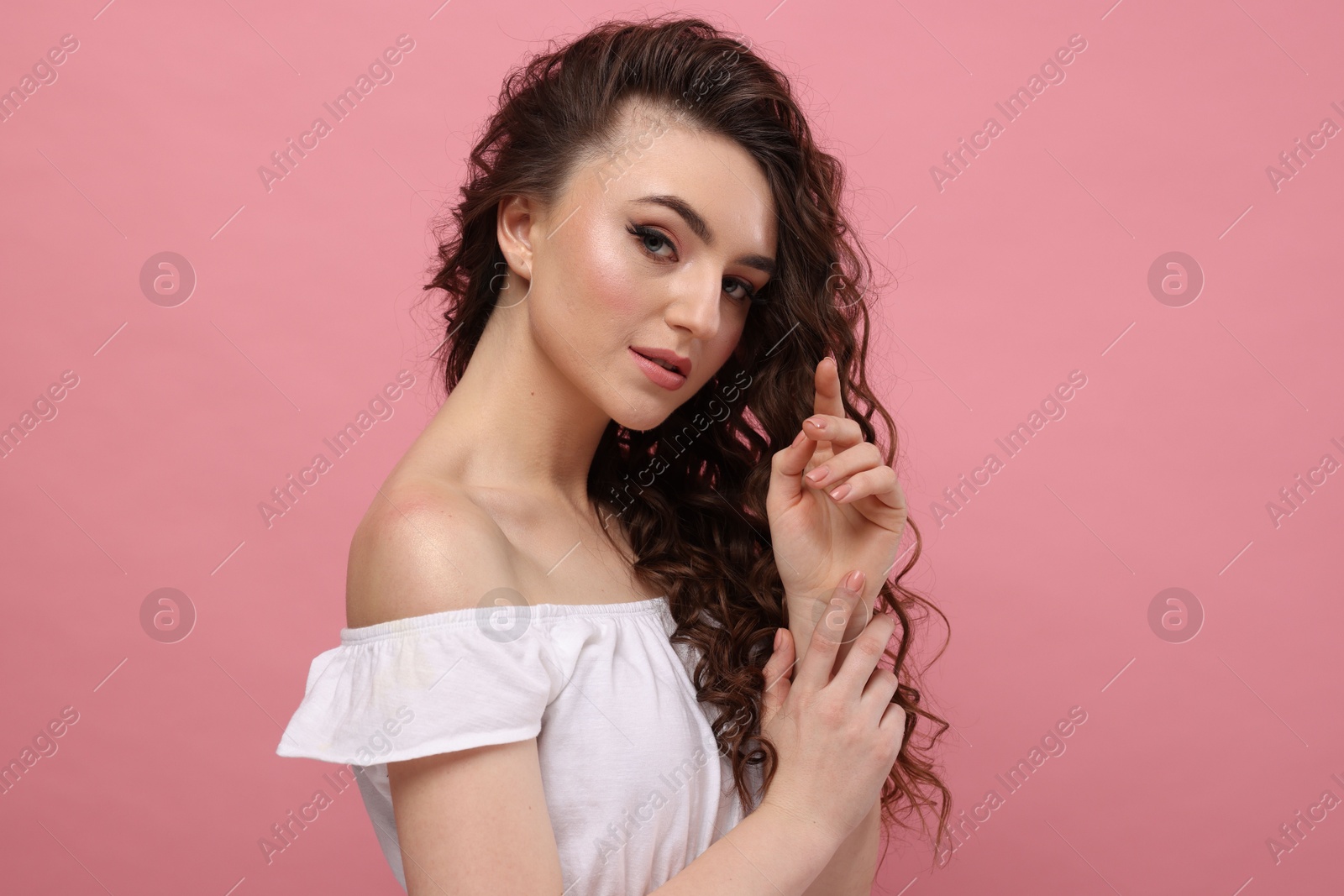 Photo of Beautiful young woman with long curly brown hair on pink background