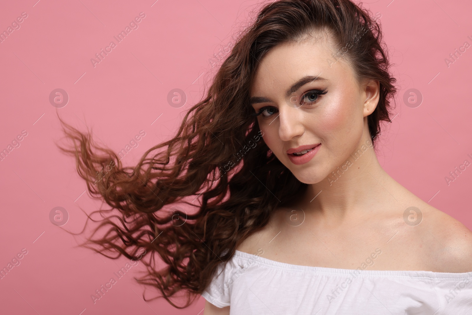 Photo of Beautiful young woman with long curly brown hair on pink background, space for text