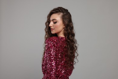 Photo of Beautiful young woman with long curly brown hair in pink sequin dress on grey background