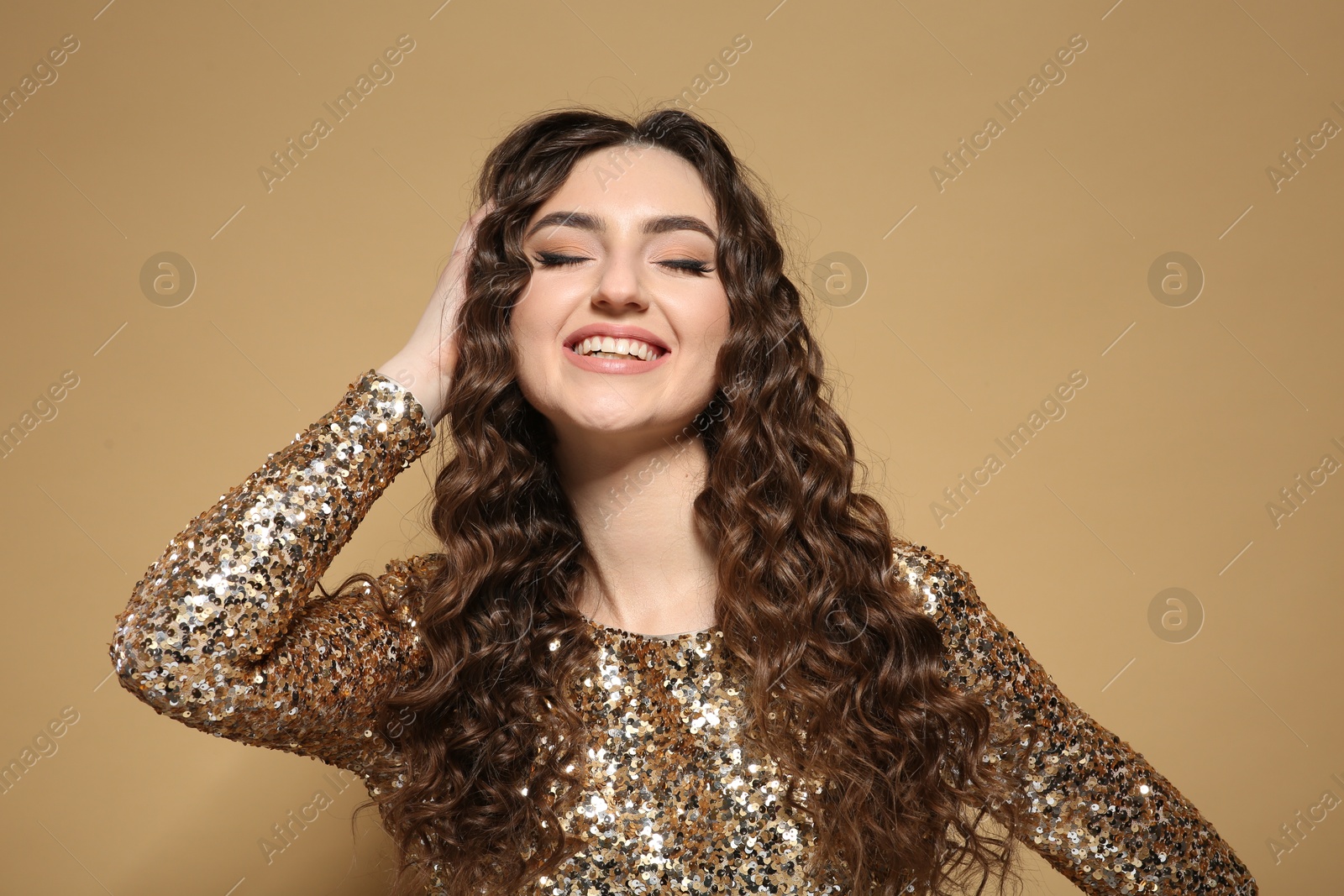 Photo of Beautiful young woman with long curly brown hair in golden sequin dress on beige background