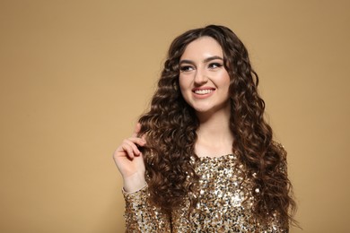 Photo of Beautiful young woman with long curly brown hair in golden sequin dress on beige background