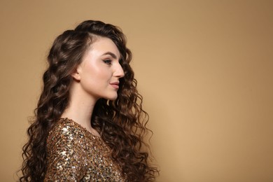 Photo of Beautiful young woman with long curly brown hair in golden sequin dress on beige background