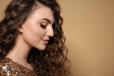 Photo of Beautiful young woman with long curly brown hair in golden sequin dress on beige background, closeup. Space for text