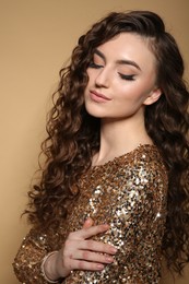 Photo of Beautiful young woman with long curly brown hair in golden sequin dress on beige background