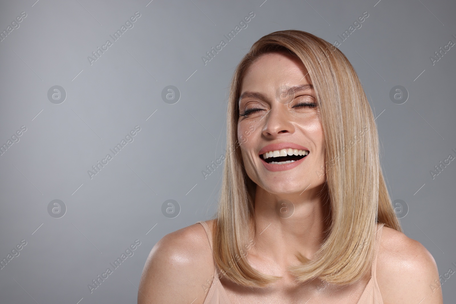 Photo of Portrait of beautiful happy woman with straight blonde hair on grey background, space for text