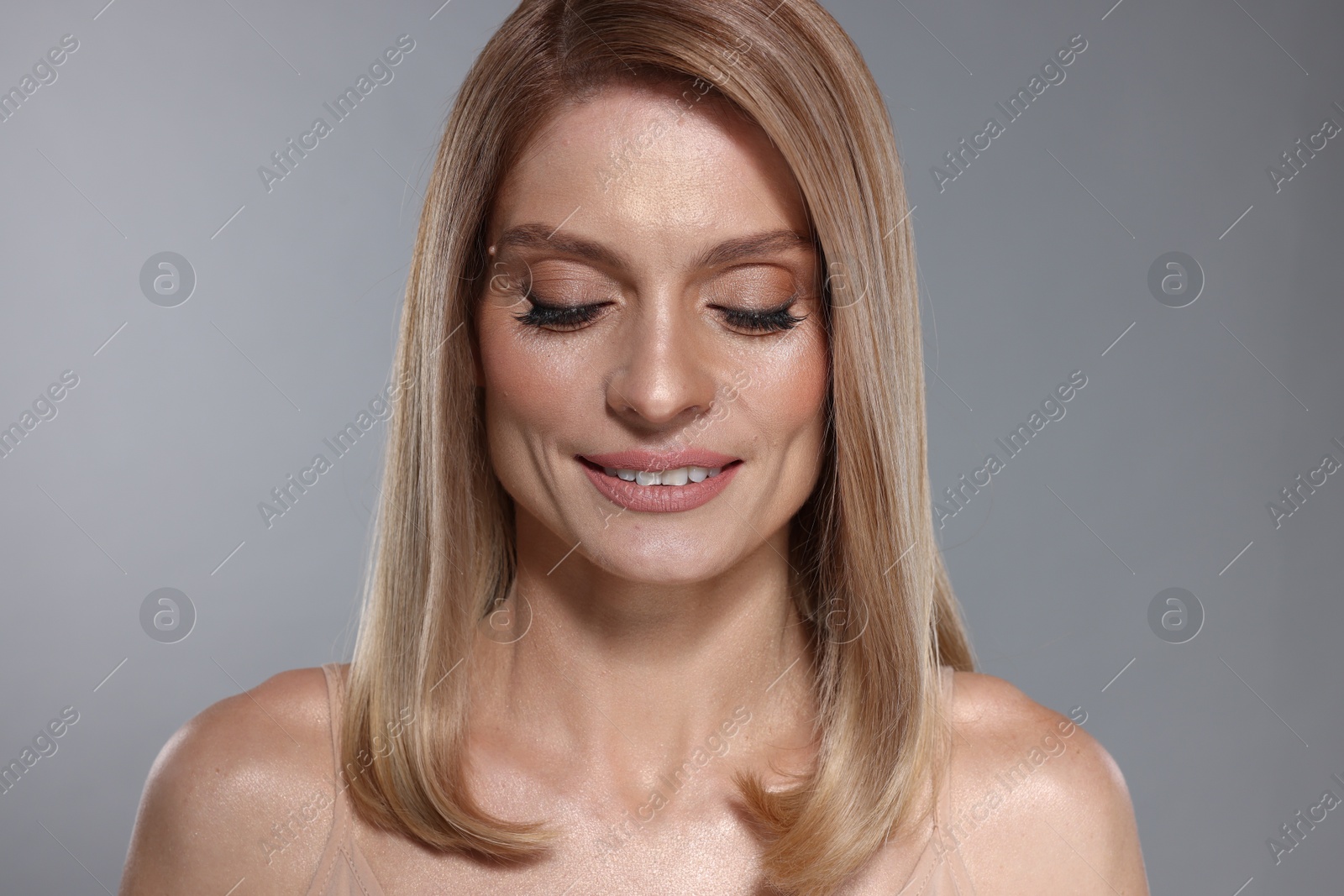 Photo of Portrait of beautiful happy woman with straight blonde hair and stylish makeup on grey background