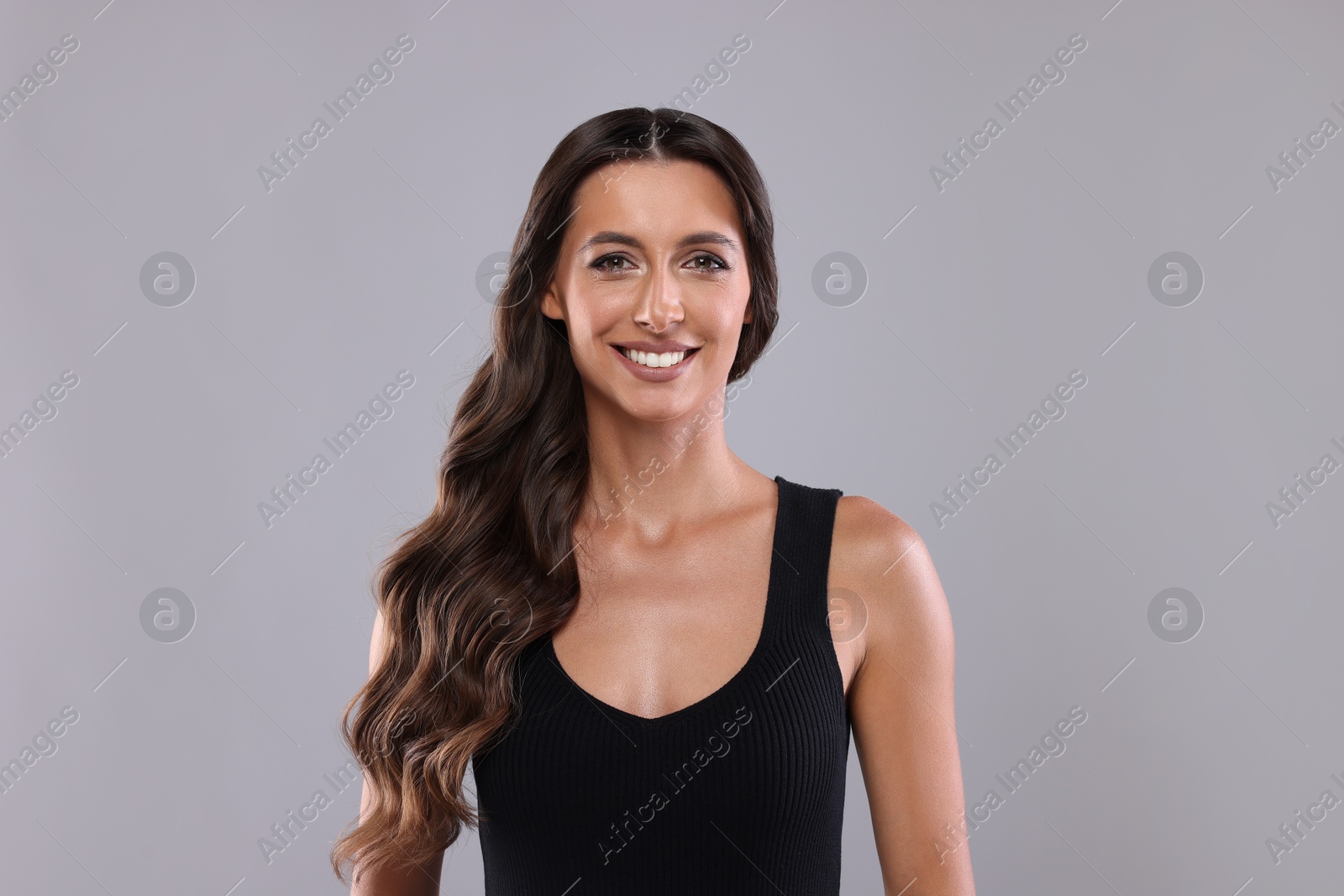 Photo of Hair styling. Portrait of beautiful woman with wavy long hair on grey background