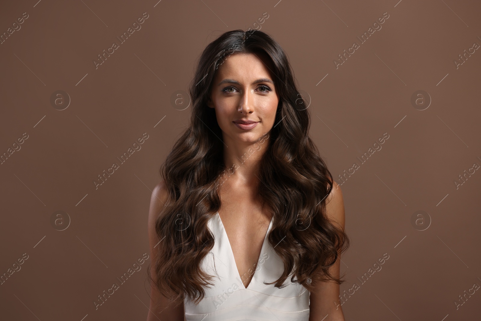 Photo of Hair styling. Portrait of beautiful woman with wavy long hair on brown background