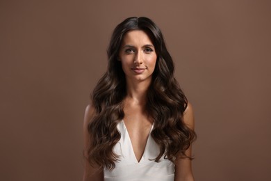 Hair styling. Portrait of beautiful woman with wavy long hair on brown background