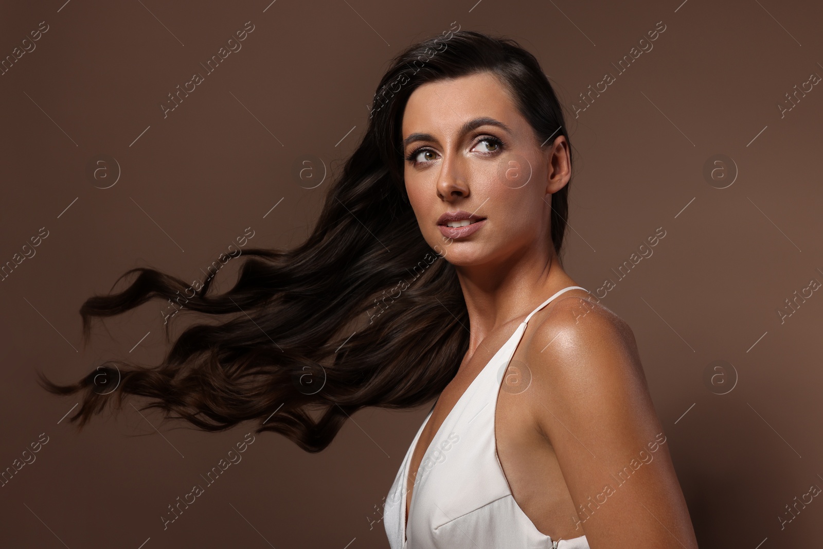 Photo of Hair styling. Beautiful woman with wavy long hair on brown background