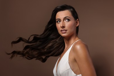 Photo of Hair styling. Beautiful woman with wavy long hair on brown background