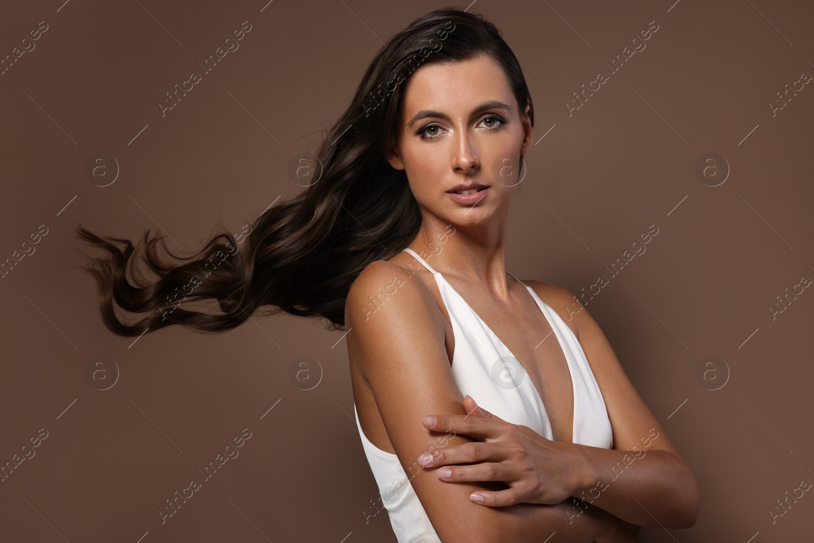 Photo of Hair styling. Portrait of beautiful woman with wavy long hair on brown background