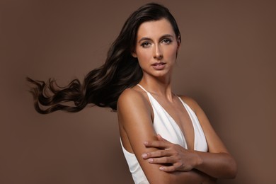 Photo of Hair styling. Portrait of beautiful woman with wavy long hair on brown background