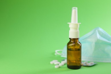 Photo of Allergy treatment. Nasal spray, pills and protective mask on green background. Space for text