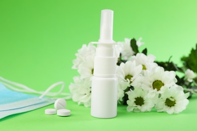 Photo of Allergy treatment. Nasal spray, pills and flowers on green background