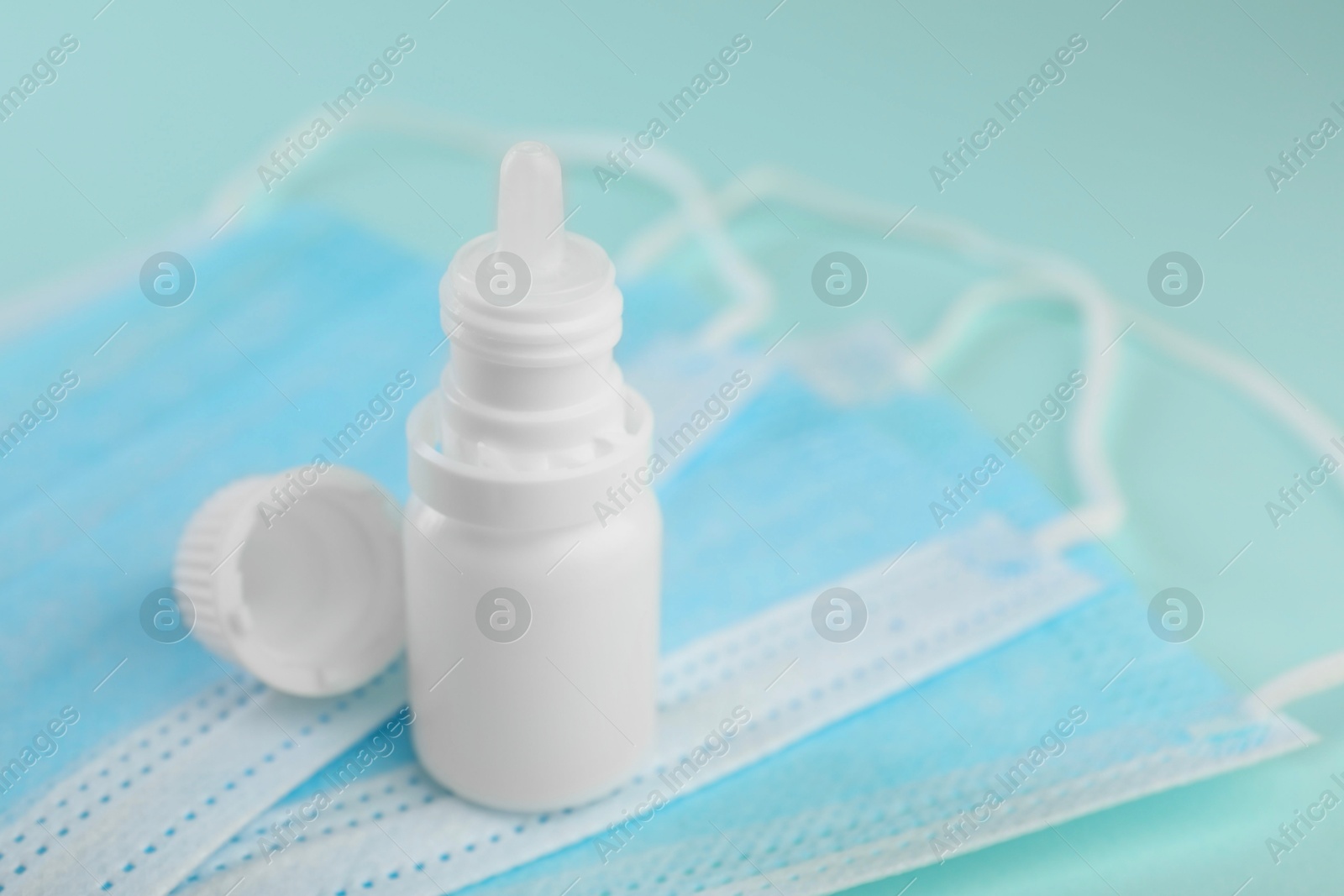 Photo of Allergy treatment. Nasal drops and protective masks on light blue background, closeup