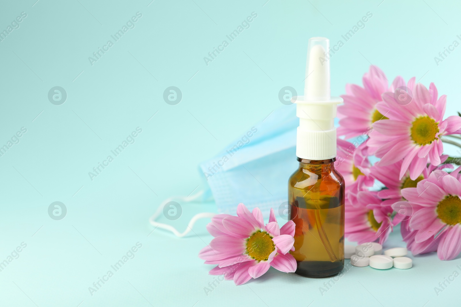 Photo of Allergy treatment. Nasal spray, pills and flowers on light blue background. Space for text