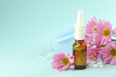 Photo of Allergy treatment. Nasal spray, pills and flowers on light blue background. Space for text