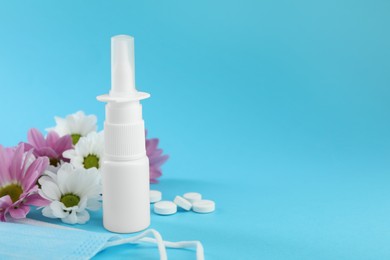 Photo of Allergy treatment. Nasal spray, pills, protective mask and flowers on light blue background. Space for text