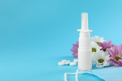 Photo of Allergy treatment. Nasal spray, pills, protective mask and flowers on light blue background. Space for text