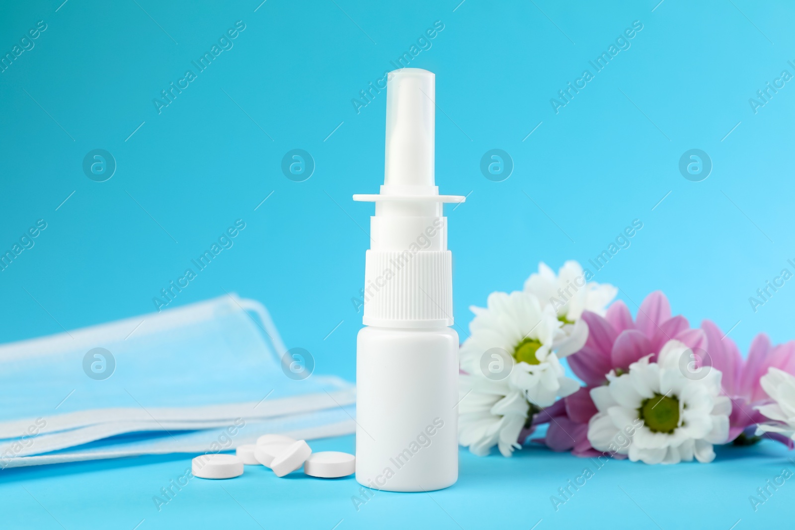 Photo of Allergy treatment. Nasal spray, pills, protective mask and flowers on light blue background