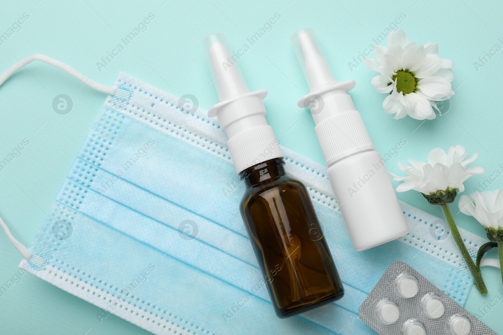 Photo of Allergy treatment. Different medications, protective mask and flowers on light blue background, flat lay