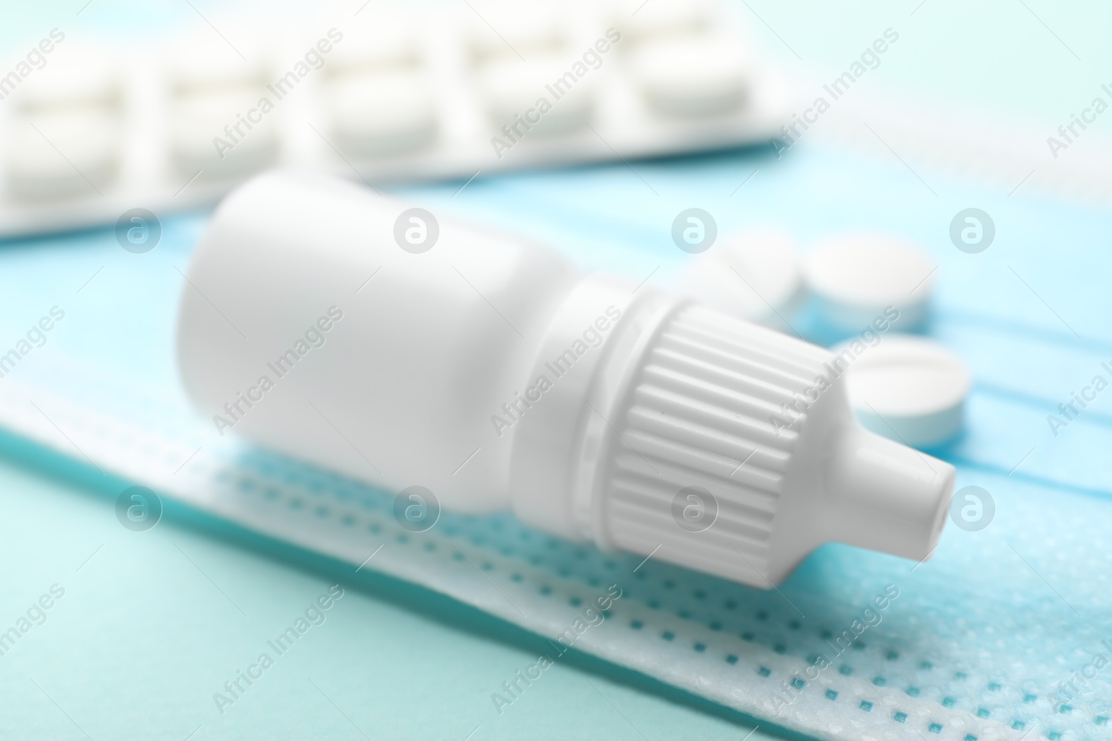 Photo of Allergy treatment. Nasal drops, pills and protective mask on light blue background, closeup