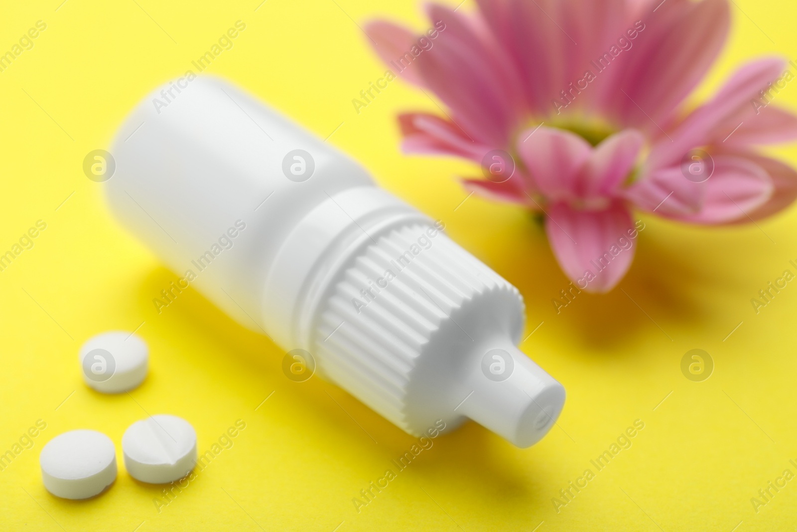 Photo of Allergy treatment. Nasal drops, pills and flower on yellow background, closeup