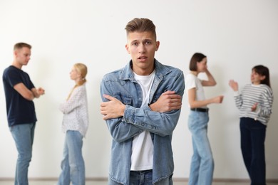 Photo of Young man feeling uncomfortable among people indoors, selective focus