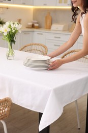 Photo of Woman putting plates on table with white tablecloth in kitchen, closeup