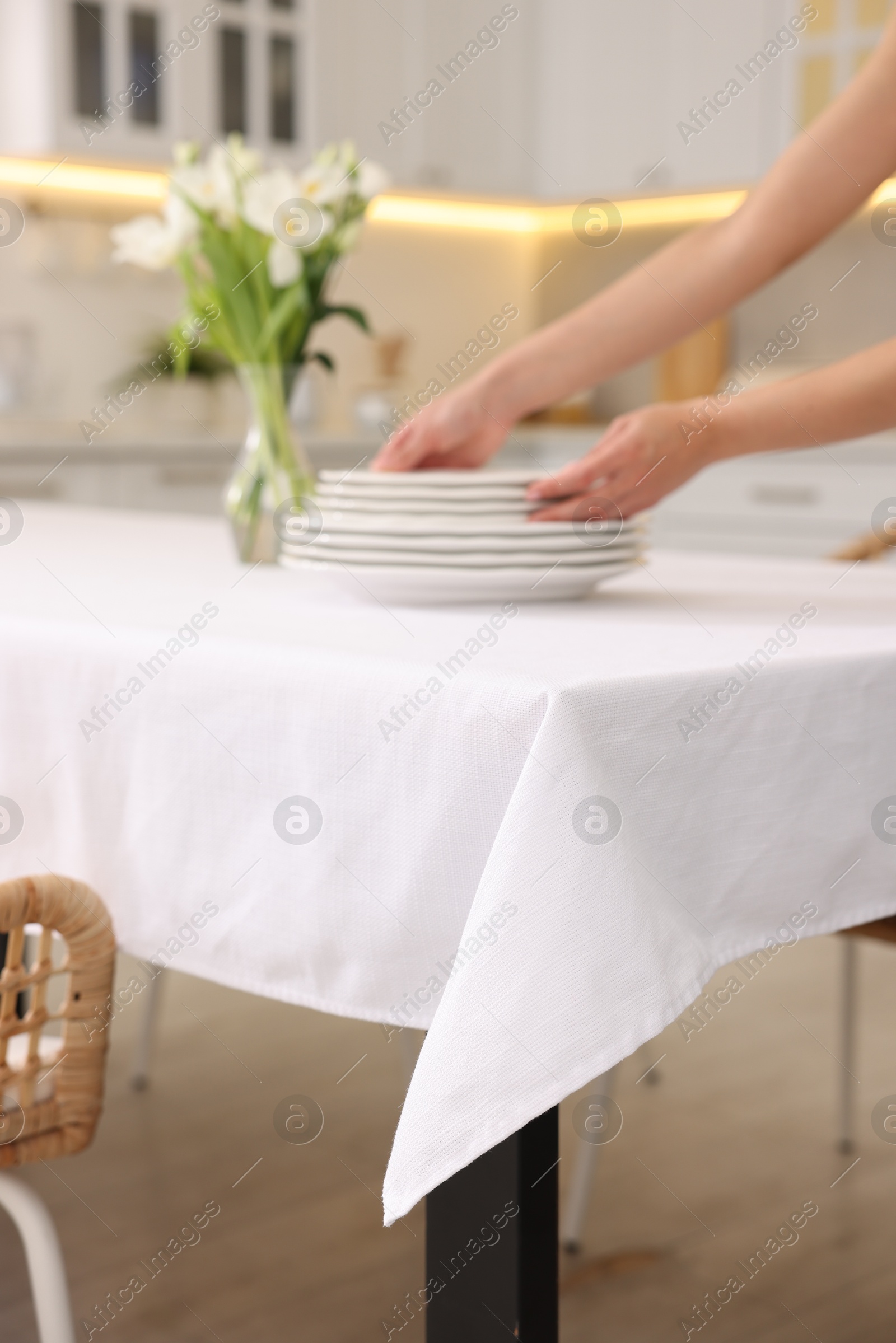 Photo of Woman putting plates on table with white tablecloth in kitchen, closeup